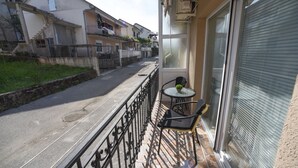 Ein Balkon mit kleinem Tisch und Stühlen, ein Fenster mit Jalousien und Blick auf angrenzende Gebäude.