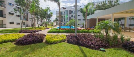 A modern hotel courtyard with a swimming pool, well-maintained lawns, and a variety of plants.