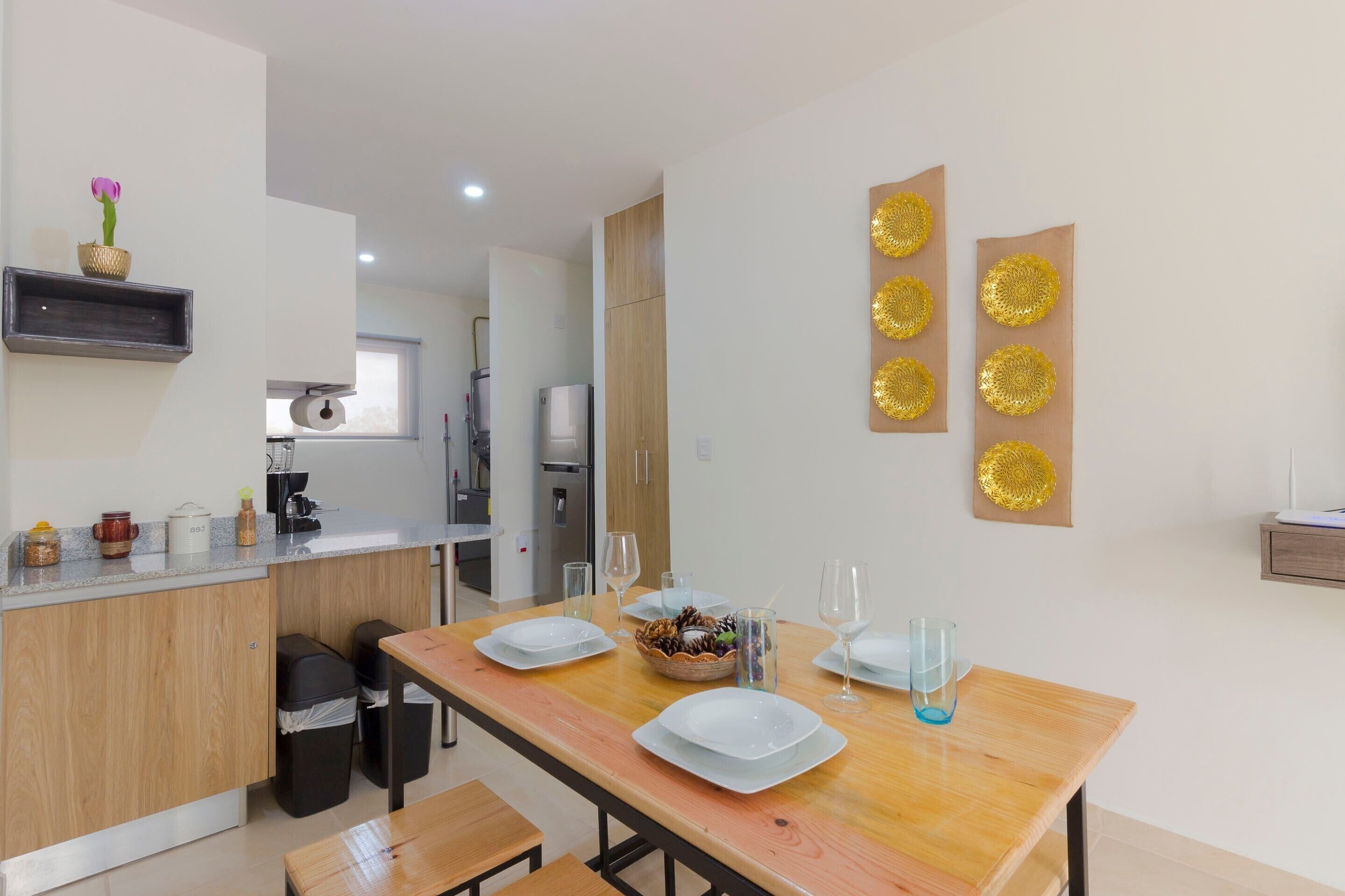A modern kitchen with wooden cabinets, a dining table set with plates and glasses, and decorative wall art.