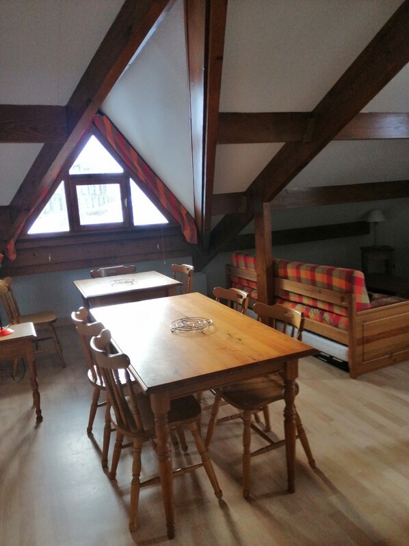 A dining area with a wooden table and chairs, a sofa with a colorful cushion, and a window with a view of buildings.