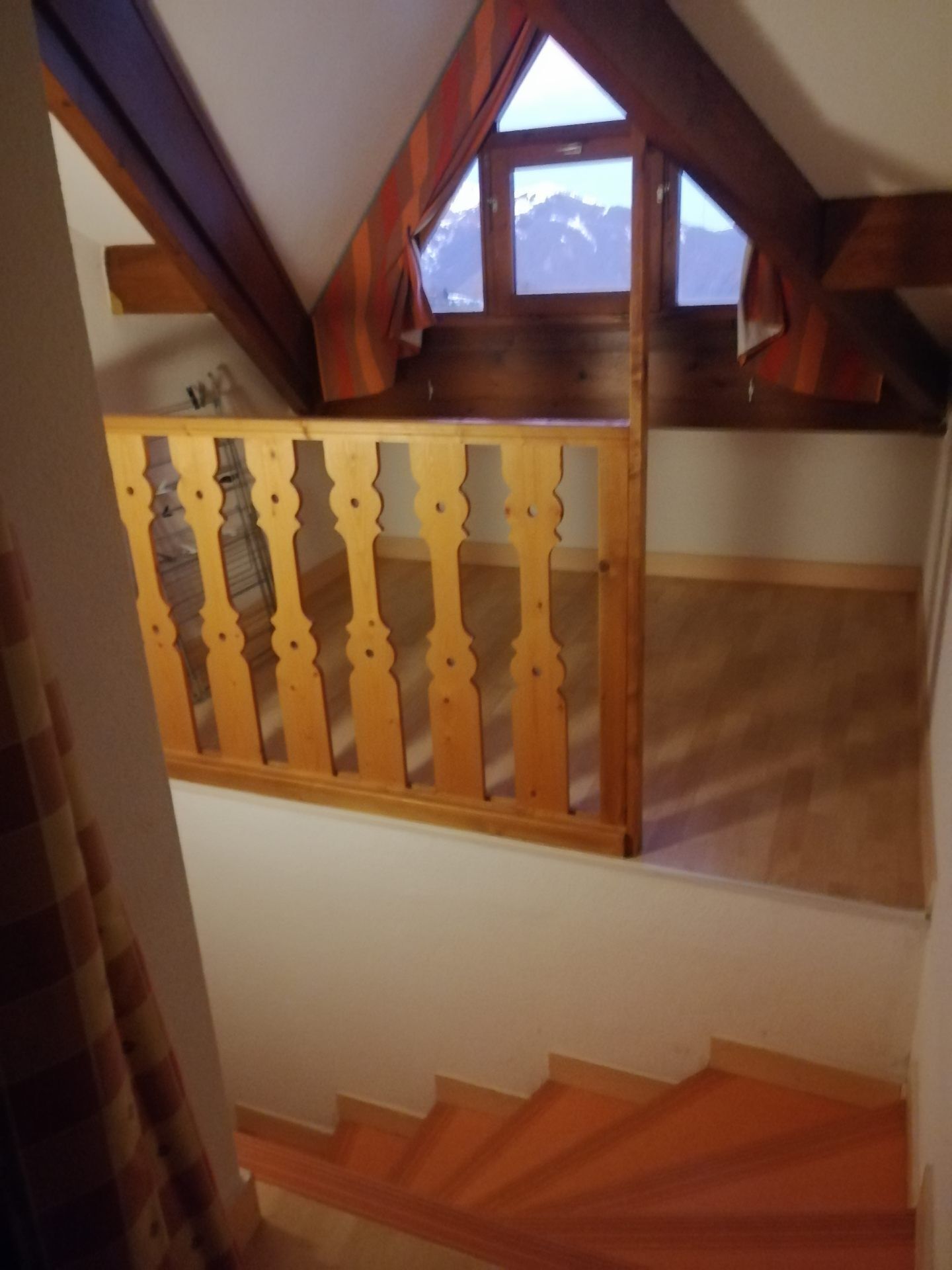 Eine Holztreppe mit Geländer, die zu einem Zimmer mit Fenster und Bergblick führt.