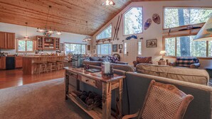 A spacious living area with wooden furniture, a dining table, and large windows offering natural light and views of the outdoors. - Relax and cozy-in with friends at this spacious Graeagle cabin (Graeagle)