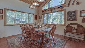 A dining area with a wooden table and chairs, large windows, and a bench with cushions. - Relax and cozy-in with friends at this spacious Graeagle cabin (Graeagle)