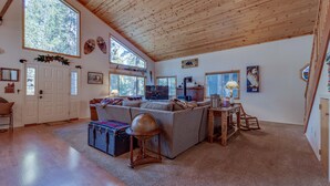 A spacious living room with a wooden ceiling, large windows, a sofa, a coffee table, and a television. - Relax and cozy-in with friends at this spacious Graeagle cabin (Graeagle)