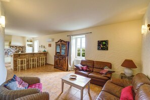 A living room with a sofa, a coffee table, a dining area with a kitchen in the background, and a window with curtains. - Mas Provence Gardoise (Uzès)- Swimming pool 12-6 m - 9 acres garden (Tresques)