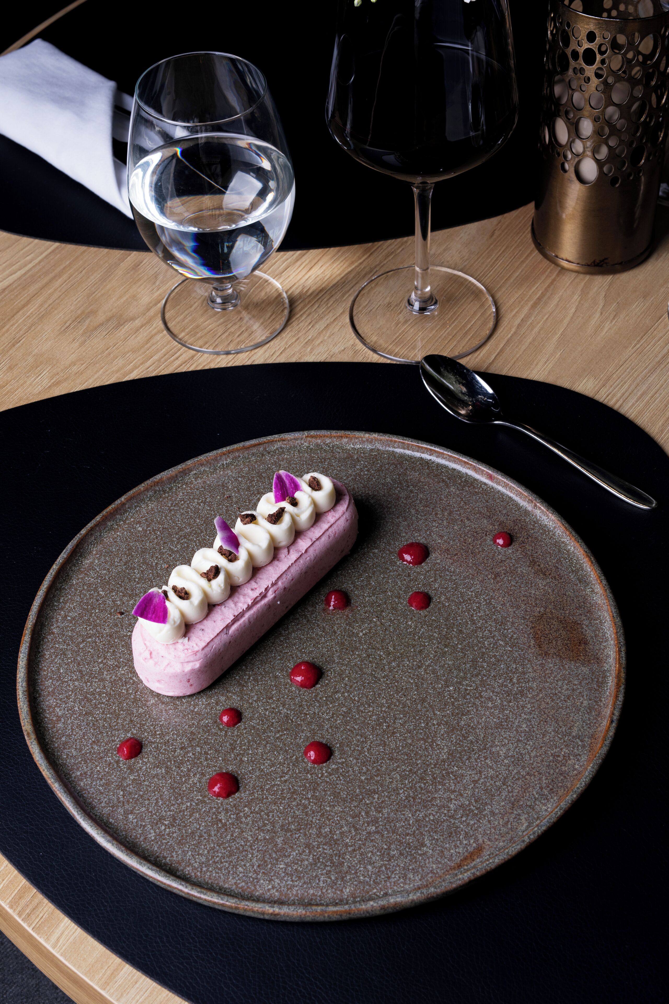 Un postre en un plato con cuchara y dos vasos de agua sobre una mesa.