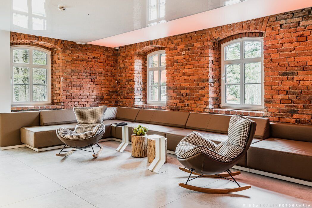 A modern interior with brick walls, large windows, and a seating area with a sofa and rocking chairs.