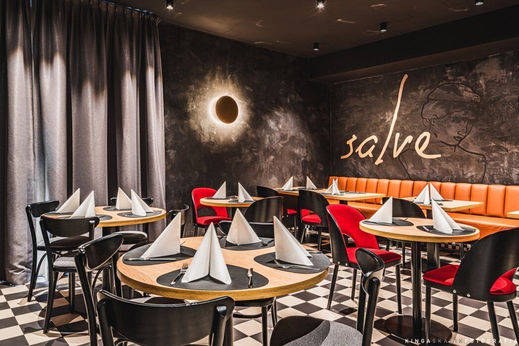 A restaurant interior with round tables, black and red chairs, and a checkered floor.