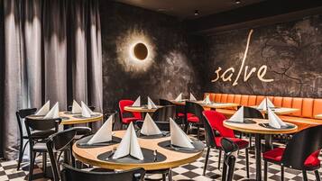 Un interior de restaurante con mesas redondas, sillas negras y rojas, y un piso a cuadros.