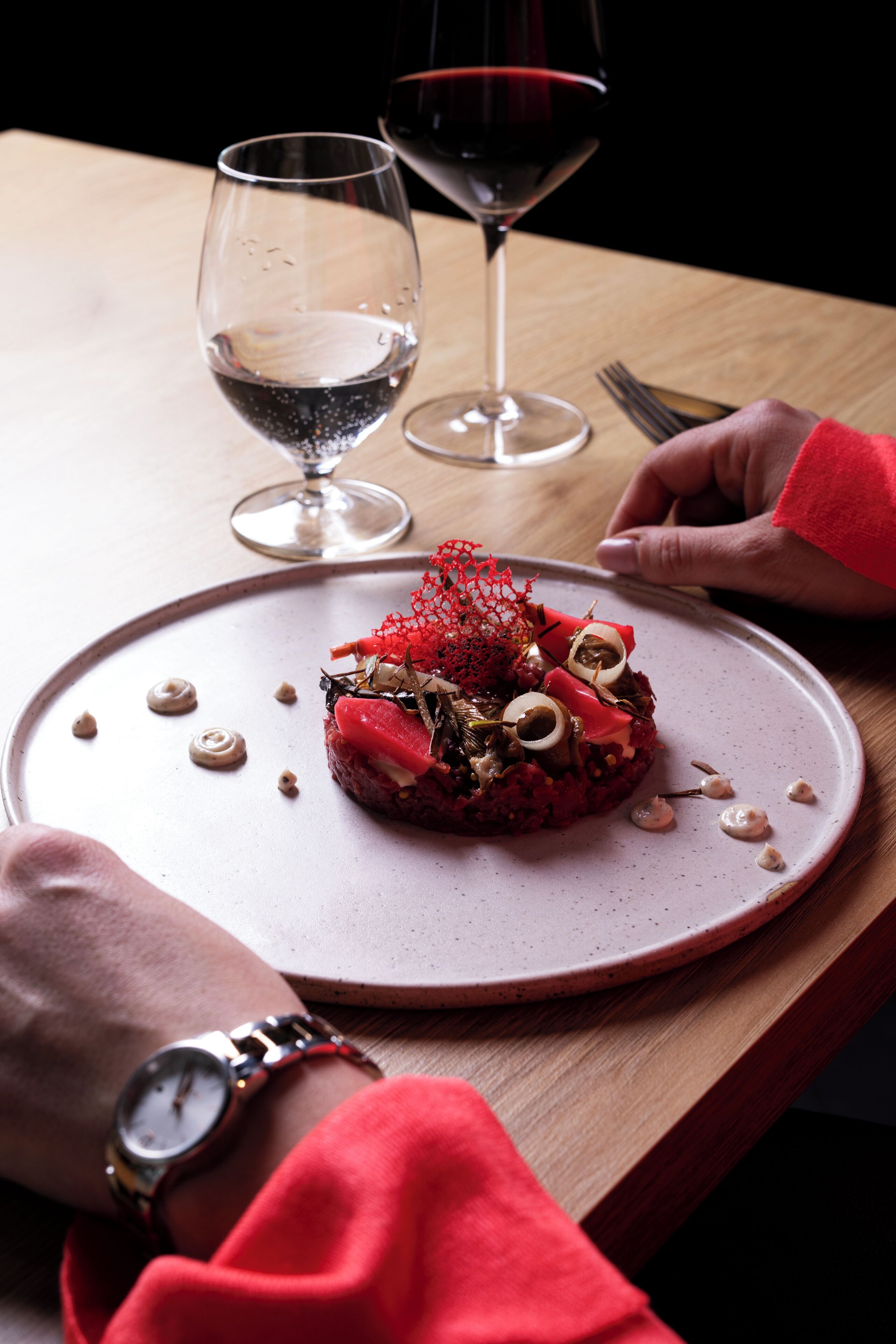 A dining table with a plate of food, two wine glasses, and a fork.