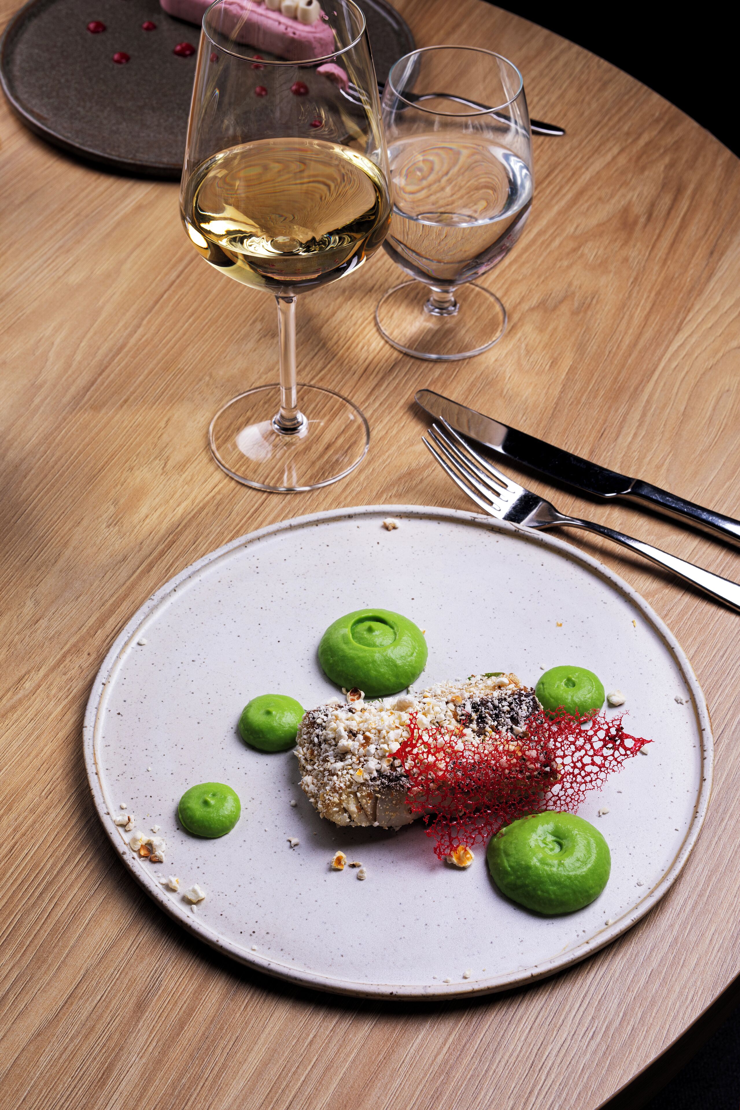 A dining table with a plate of food, a glass of white wine, and cutlery.