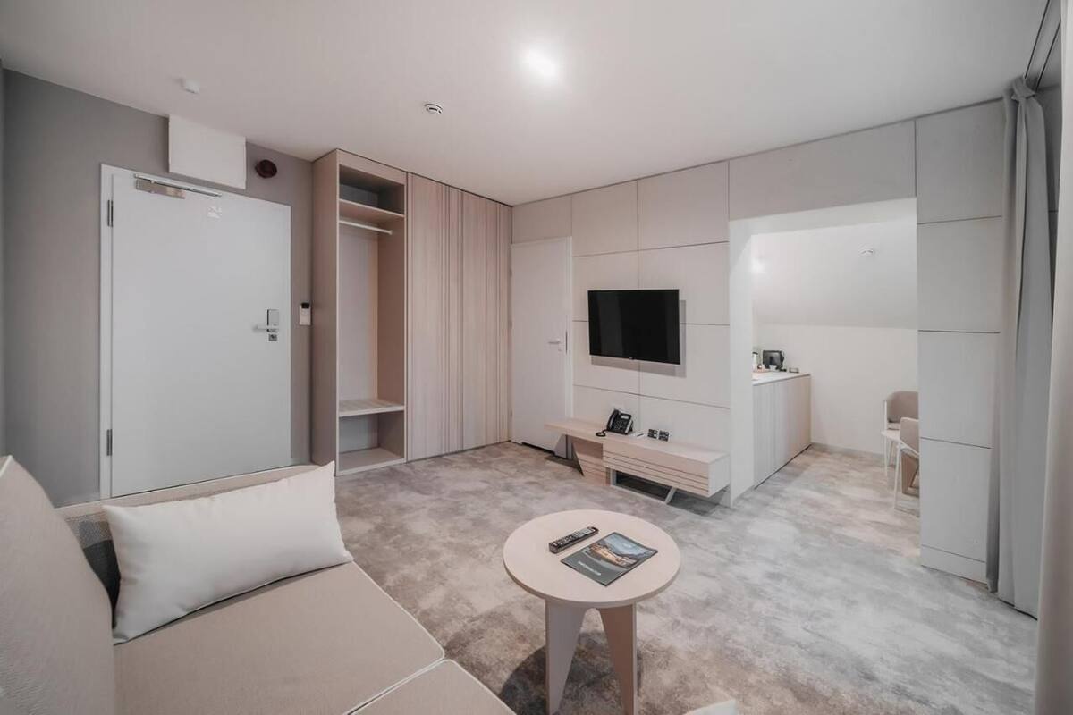 A modern, well-lit room with a sofa, a small round table, a TV, and a wardrobe.