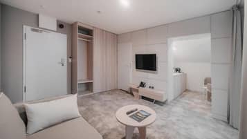 A modern, well-lit room with a sofa, a small round table, a TV, and a wardrobe.