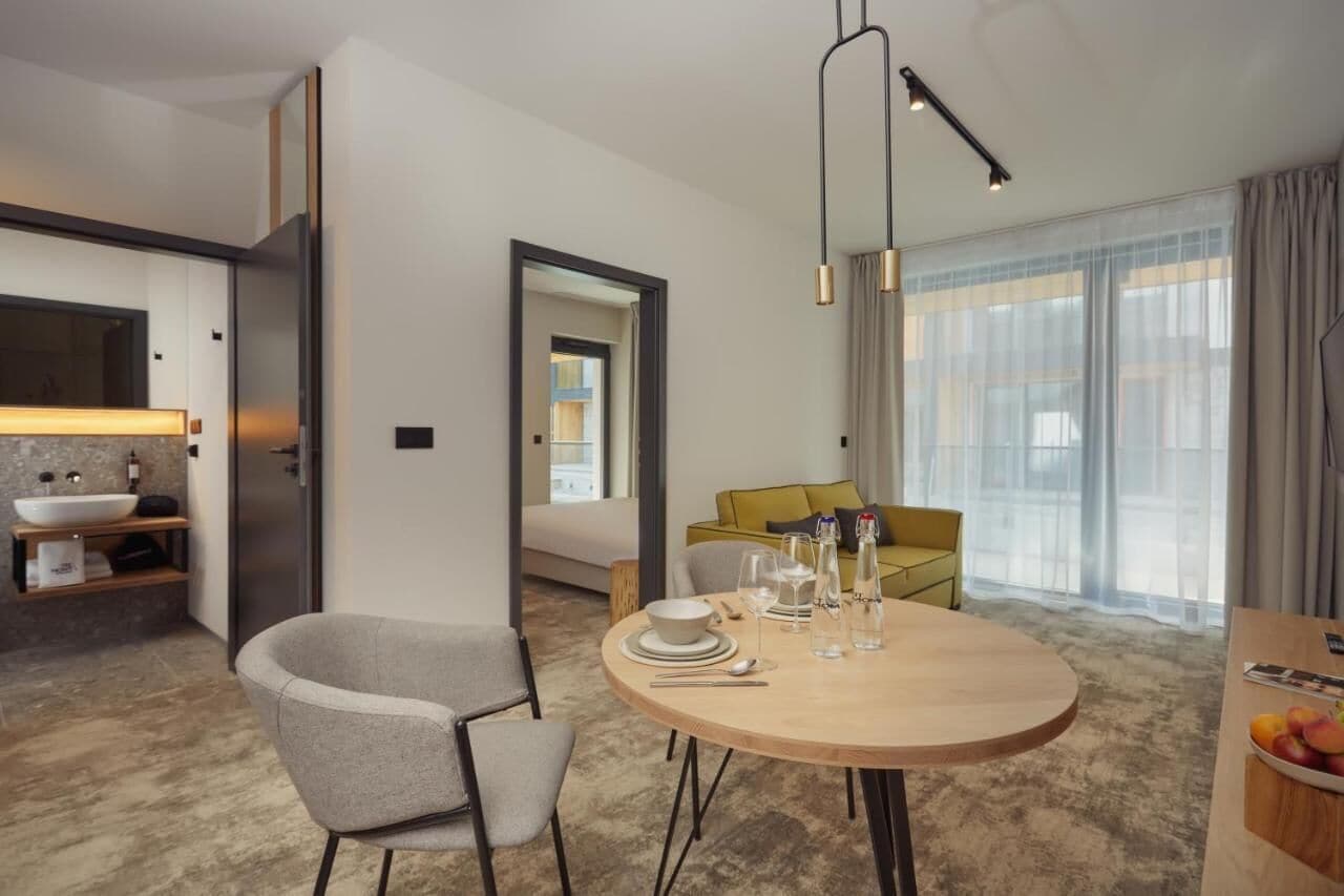 Una habitación de hotel moderna con una mesa redonda de comedor, un sofá y un ventanal con cortinas.