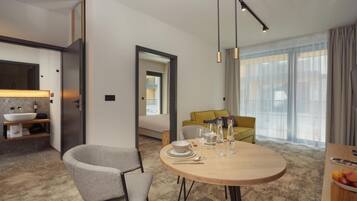 Una habitación de hotel moderna con una mesa redonda de comedor, un sofá y un ventanal con cortinas.