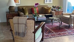 Un salon comprenant un canapé, des fauteuils, une table basse et un tapis. Des tableaux encadrés ornent le mur, et une lampe est posée sur une table d’appoint.