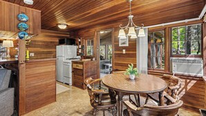 L’intérieur d’un chalet en bois comprend une table à manger, des chaises, un coin cuisine et de grandes fenêtres.