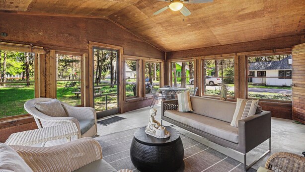 Une pièce spacieuse avec un plafond en bois, de grandes fenêtres, un canapé, des fauteuils et une table décorative.