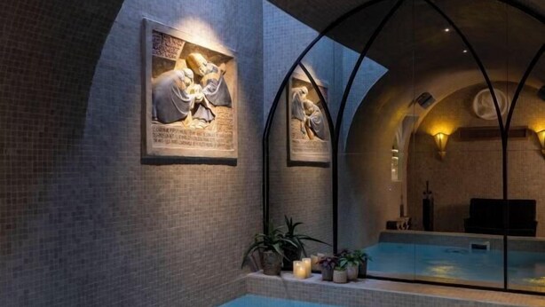 Un espace de bien-être comprenant une piscine, des murs en pierre et deux sculptures murales éclairées.