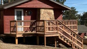 Eine Blockhütte mit einem Steinkamin, einer Holzdar Terrasse und einer Treppe zum Eingang.