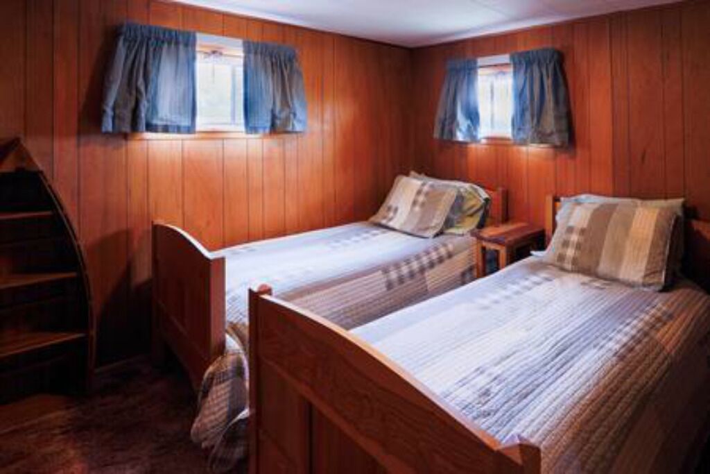 A room with two wooden beds, a ladder, and a window with curtains.