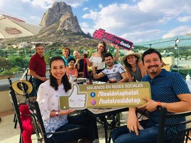 Un grupo de personas sentadas en una mesa con un cartel que promociona un restaurante y nombres de usuario en redes sociales.
