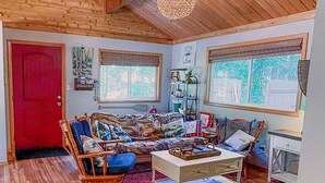 A cozy living room with wooden floors, a red door, a rocking chair, a sofa, a coffee table, and a hanging light fixture.