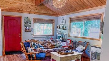 A cozy living room with wooden floors, a red door, a rocking chair, a sofa, a coffee table, and a hanging light fixture.
