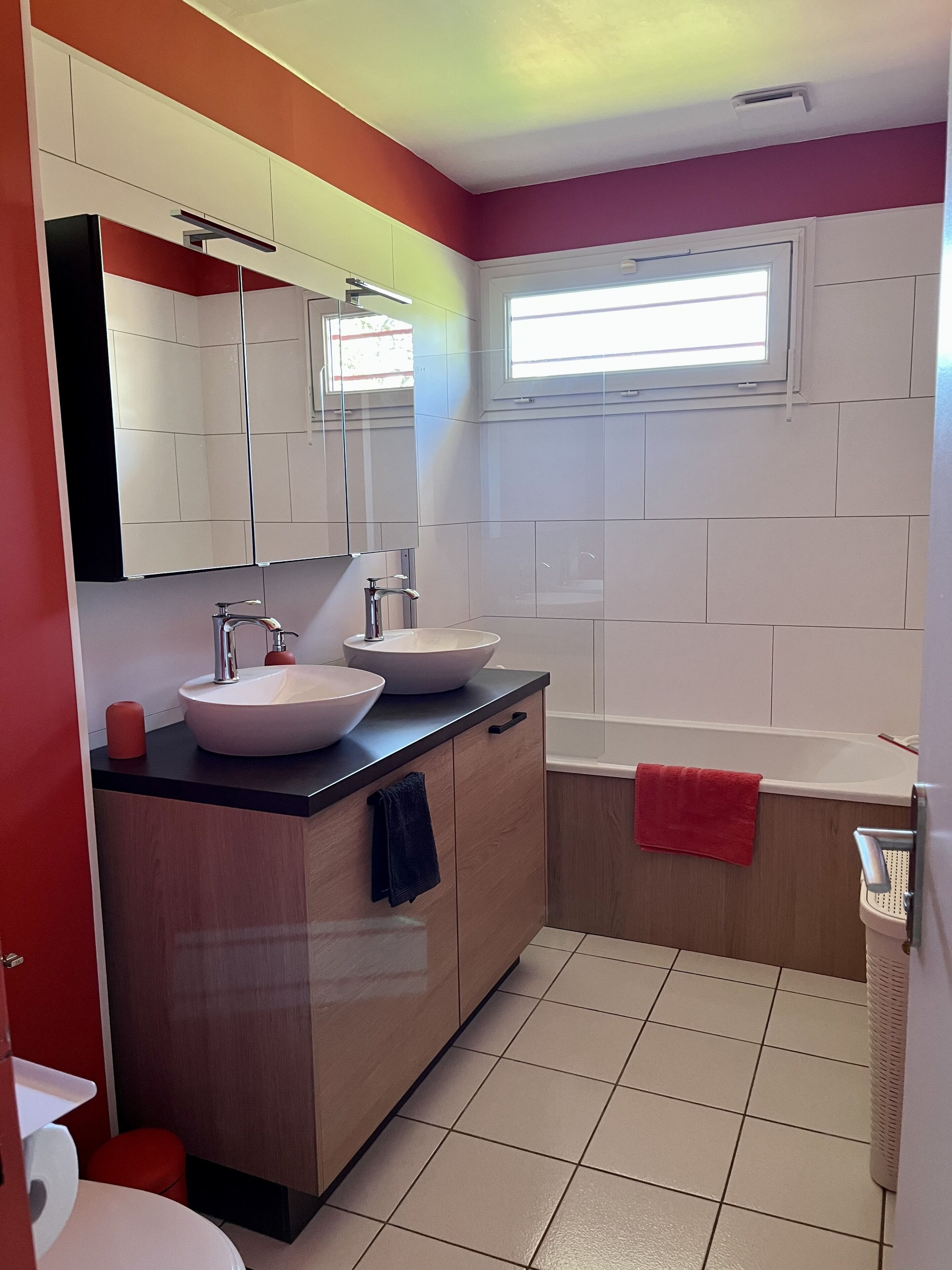 Ein modernes Badezimmer mit zwei Waschbecken, einem großen Spiegel und einem Fenster.
