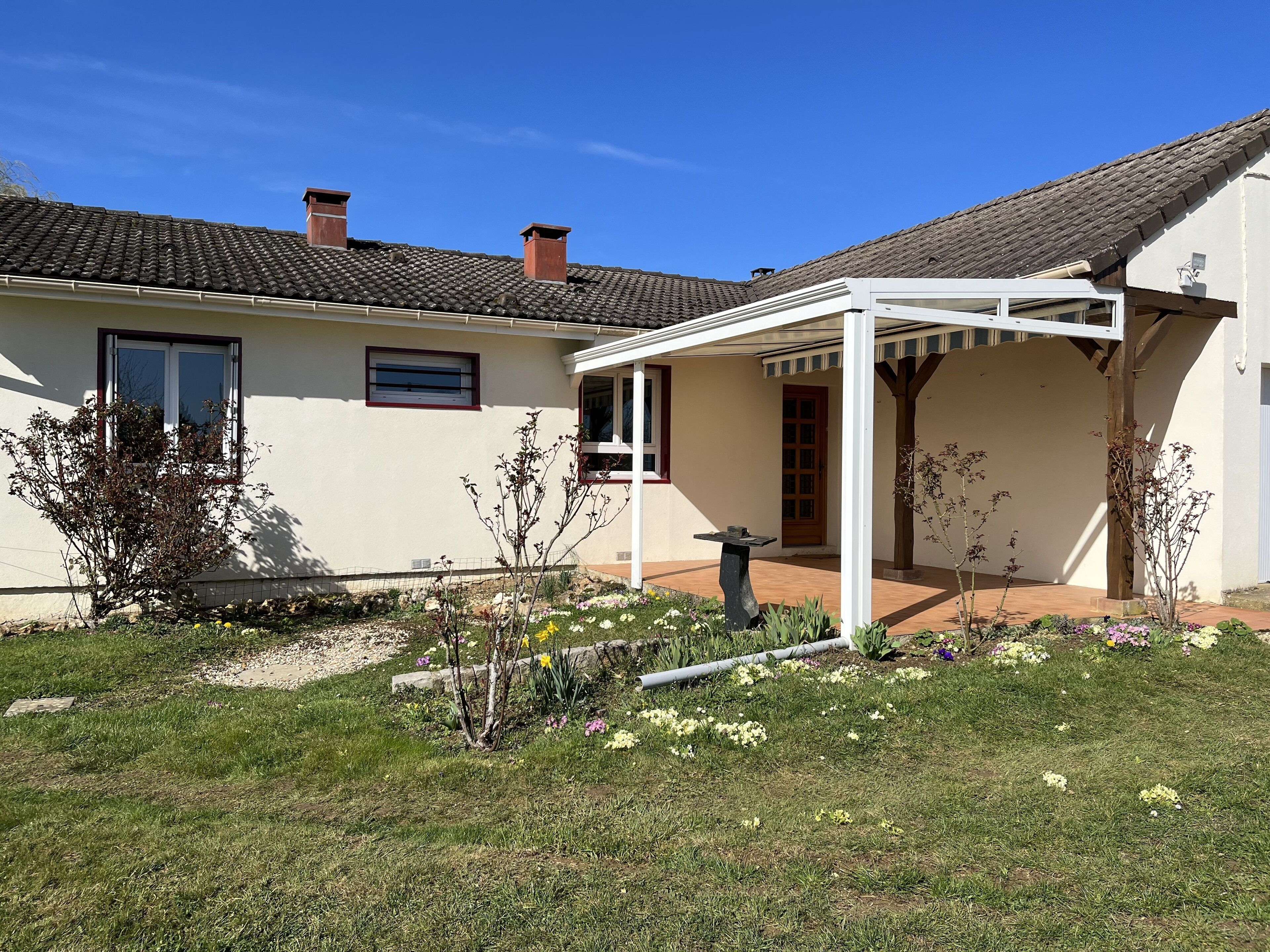 A house with a tiled roof, a covered patio, and a garden with various plants and flowers.