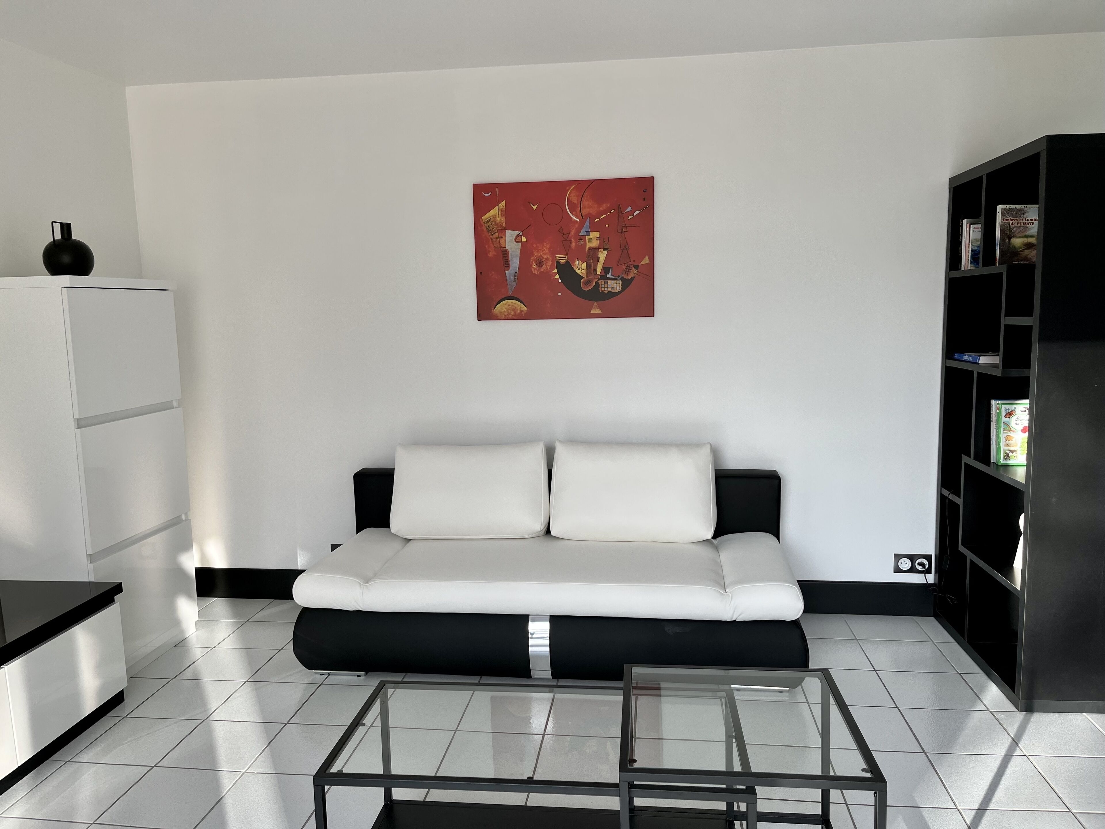 Un salon moderne avec un canapé blanc, une table basse en verre, une bibliothèque noire et un réfrigérateur blanc.