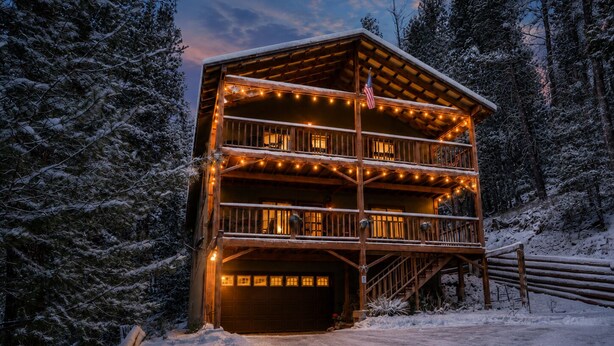 A multi-story wooden cabin with balconies, surrounded by snow-covered trees.