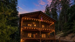 A two-story wooden cabin with a balcony, string lights, and an American flag.