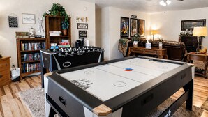 A pool table with a foosball table, a bookshelf, a coffee table, and a ceiling fan in a living room.