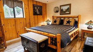 A wooden-paneled room with a bed, a bench, a lamp, and artwork on the walls.