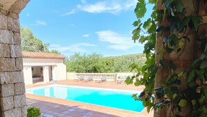 Eine Steinterrasse mit Pool, Sitzgelegenheiten und Grünpflanzen.