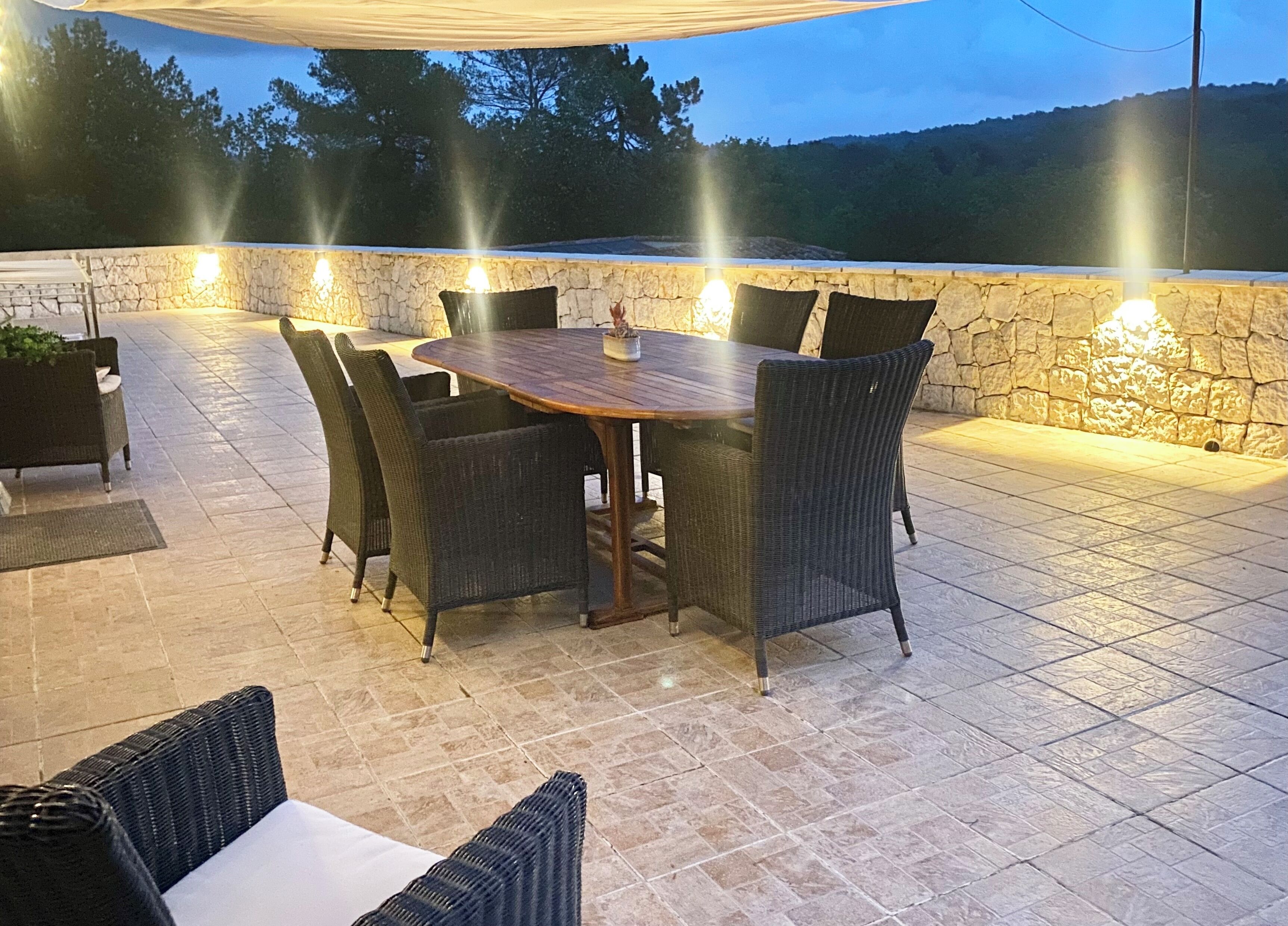 Une terrasse extérieure avec un mur en pierre, une table en bois et des chaises en osier.