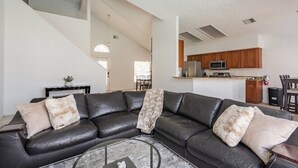 Una sala de estar moderna con un sofá de cuero negro, una mesa de centro de vidrio y una escalera que sube a otro nivel.