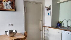 A compact kitchen with a wooden table, a metal bowl, a white dishwasher, and a door leading to another room. - Spacious Living in a small 50s villa with large garden and fireplace (Langen (Hessen))