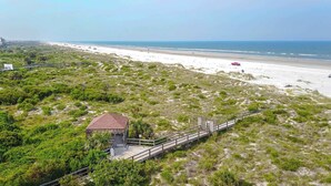 A coastal landscape with a beach, a small structure with a red roof, and a wooden boardwalk leading to it. - Ocean View Condo in St. Augustine (Saint Augustine)