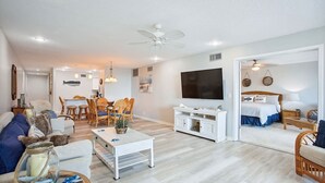A spacious living room with a dining area, a TV mounted on the wall, and a bedroom with a bed and a nightstand. - Ocean View Condo in St. Augustine (Saint Augustine)