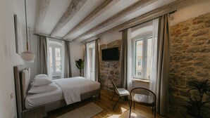 A bedroom with a bed, a desk, a chair, a TV, and a stone wall. - Porto Nativo Split (Split)