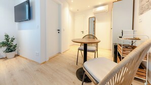A modern living room with a flat-screen TV, a round wooden table, a wicker chair, and a built-in bookshelf. - Porto Nativo Split (Split)