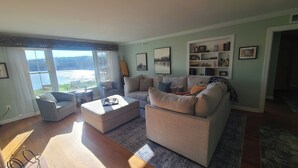 Una sala de estar con sofá, reposapiés y sillón, una estantería y un ventanal con vistas.