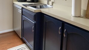 Une cuisine avec des meubles de couleur bleu foncé, un plan de travail blanc, une machine à café, une bouilloire, un évier et un porte-serviettes en papier.
