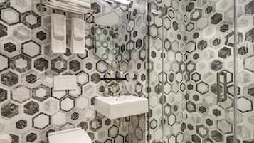 A bathroom with hexagonal patterned tiles, a white sink, a glass shower enclosure, and a toilet.