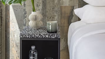 Un dormitorio moderno con una cama, una mesita de noche con una planta, un florero y una botella de agua.