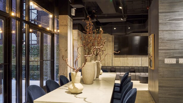 A modern dining area with a long table, blue chairs, and decorative vases.