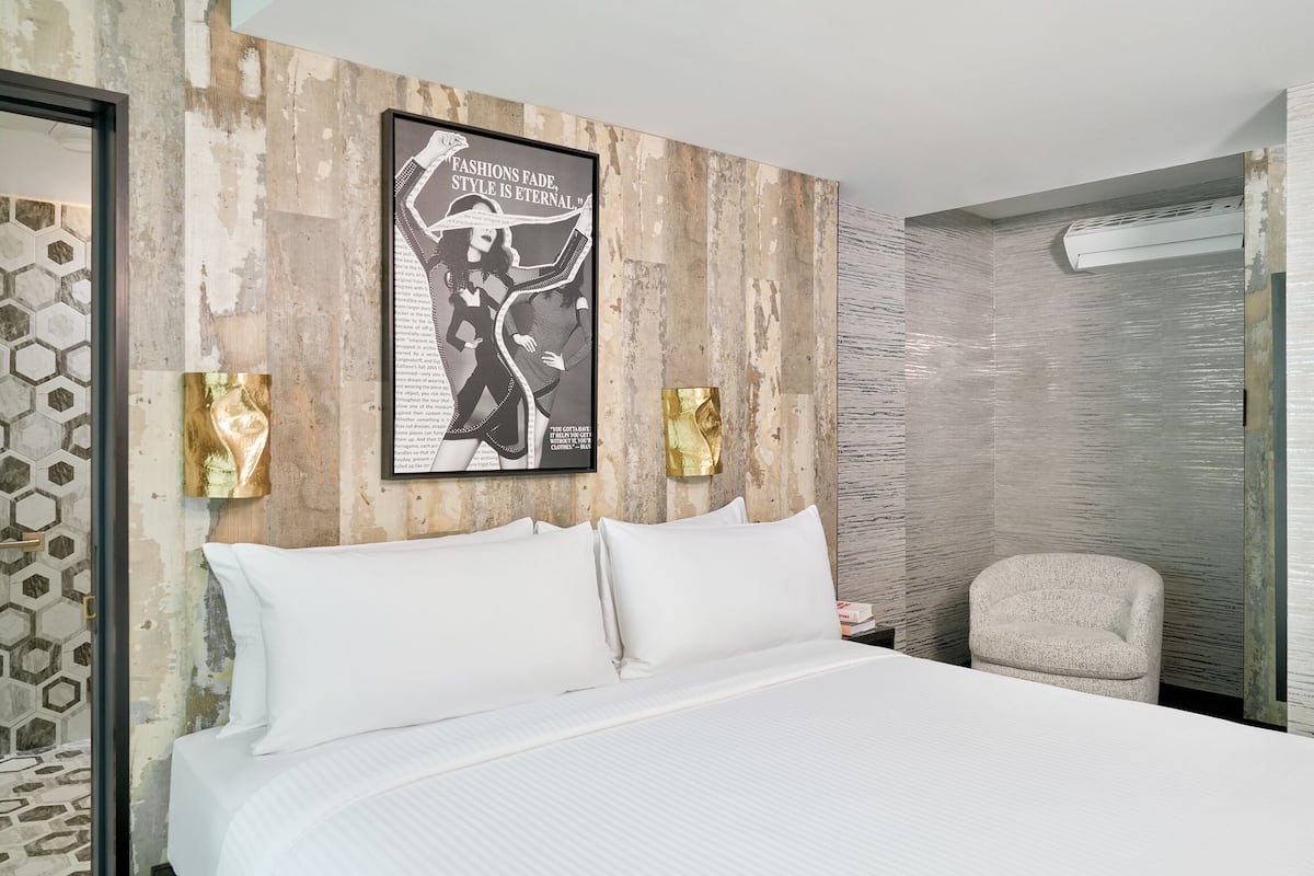 A hotel room with a large bed, a poster on the wall, and a chair.