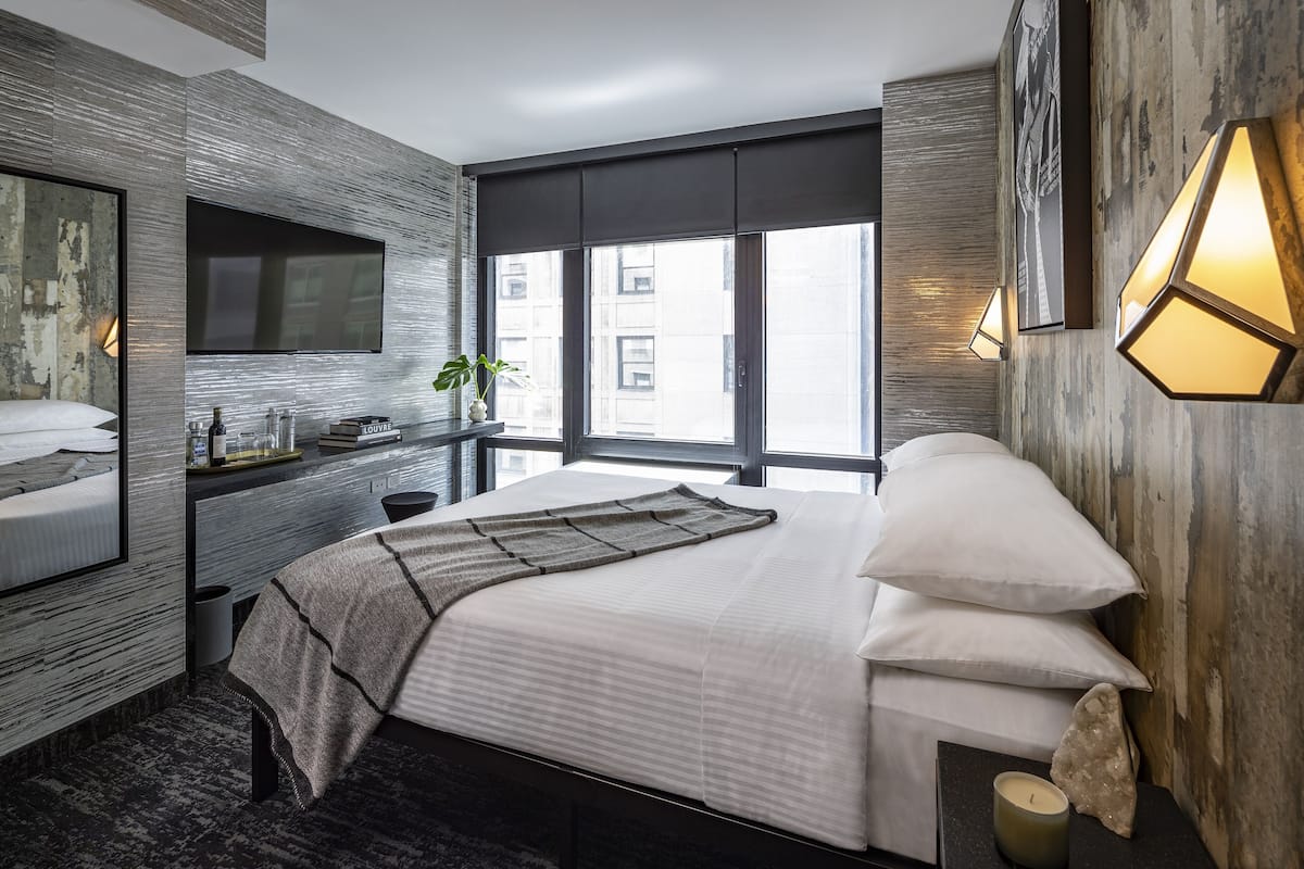 A modern bedroom with a large bed, a TV, and a window with a city view.